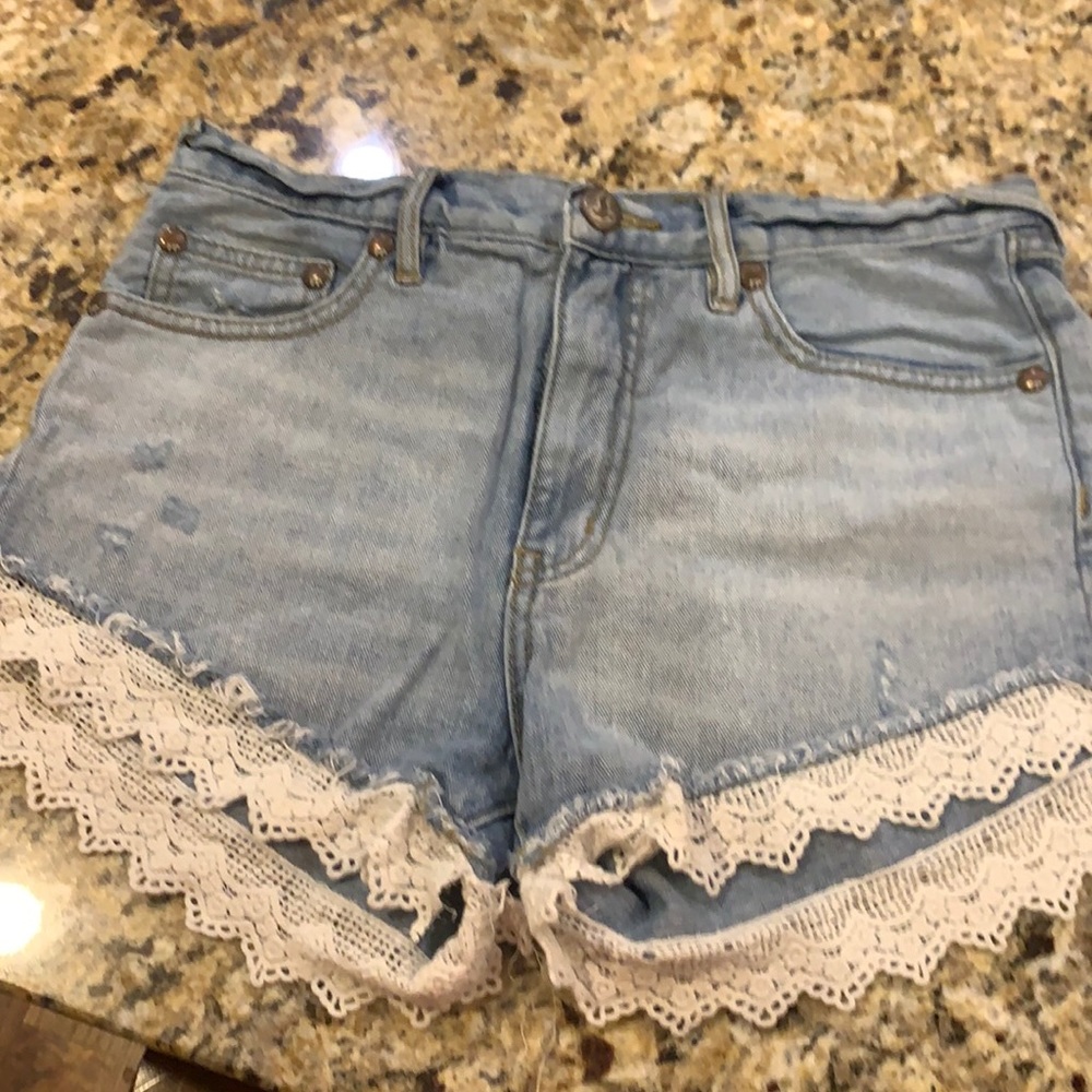 Free People light wash distressed jean shorts with beige lace.